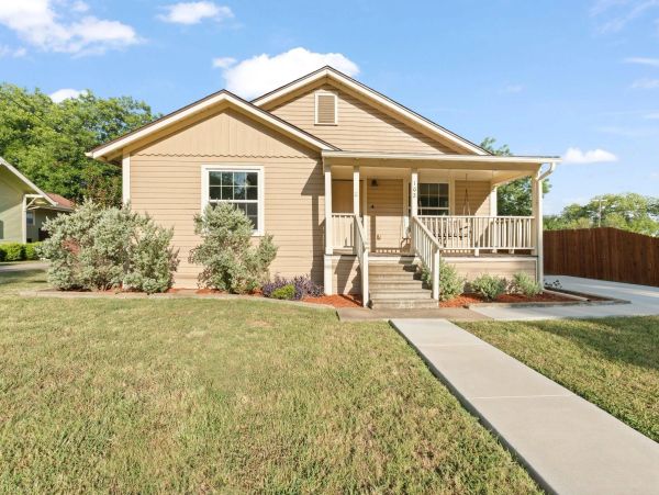 Small beige house with a front porch and lawn.