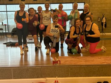Group of women in workout clothes posing with small weights and medicine balls.