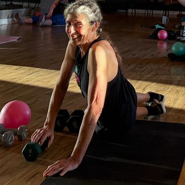 Elderly woman exercising with weights and yoga mat.