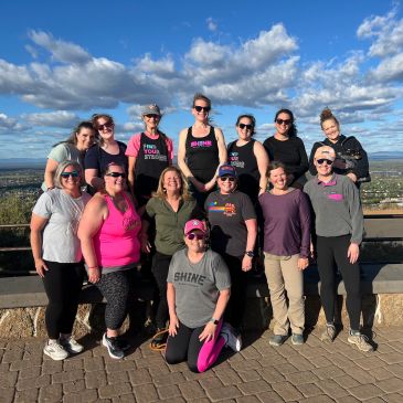 Group of women posing outdoors with a scenic sky background.