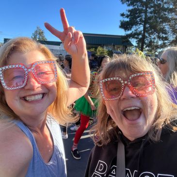 Two women smiling and wearing large pink sunglasses.