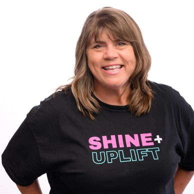 Smiling woman wearing black 'SHINE + UPLIFT' t-shirt.