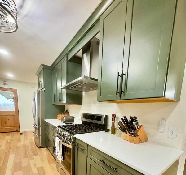 Modern kitchen with green cabinets and stainless steel appliances.