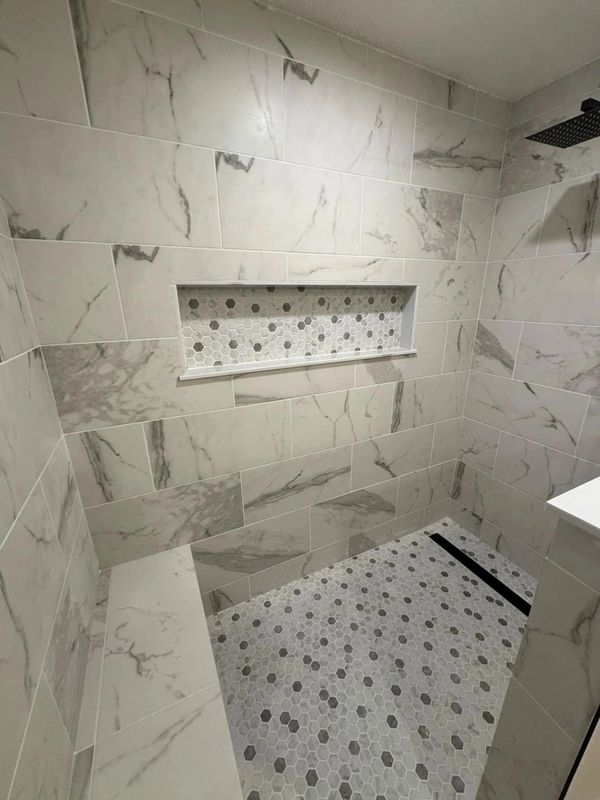 Modern shower with marble tiles and hexagonal mosaic floor.