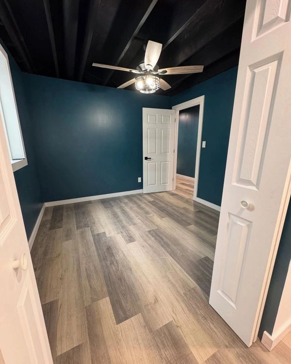 Empty room with teal walls, wood-like flooring, and a ceiling fan.