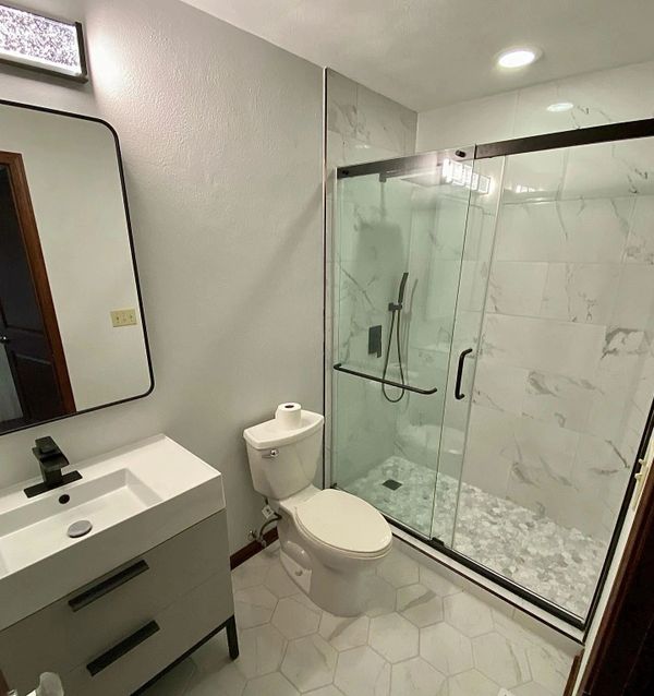Modern bathroom with glass shower, white toilet, and minimalist sink with black fixtures.