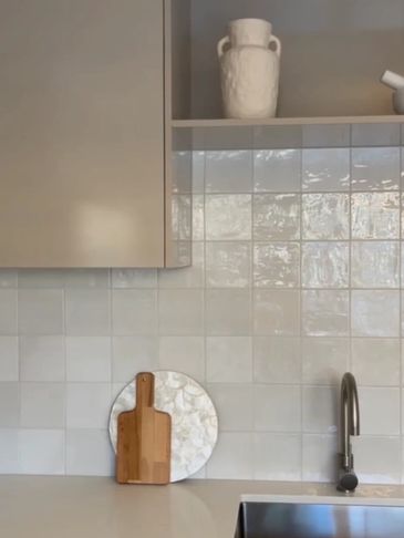 Modern kitchen corner with beige cabinets, tiled backsplash, and stainless steel sink.