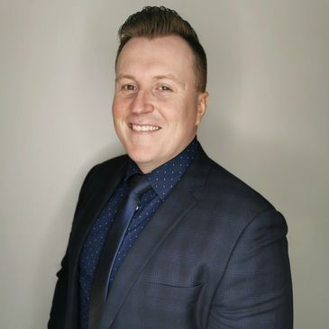 Man in a dark suit smiling against a plain background.