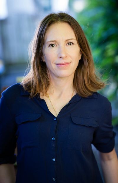 Woman with light brown hair wearing a navy blue shirt, smiling softly.