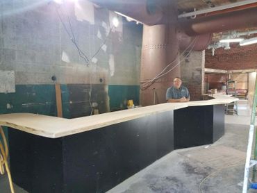 A man sitting behind a large, curved counter in a rustic indoor space.