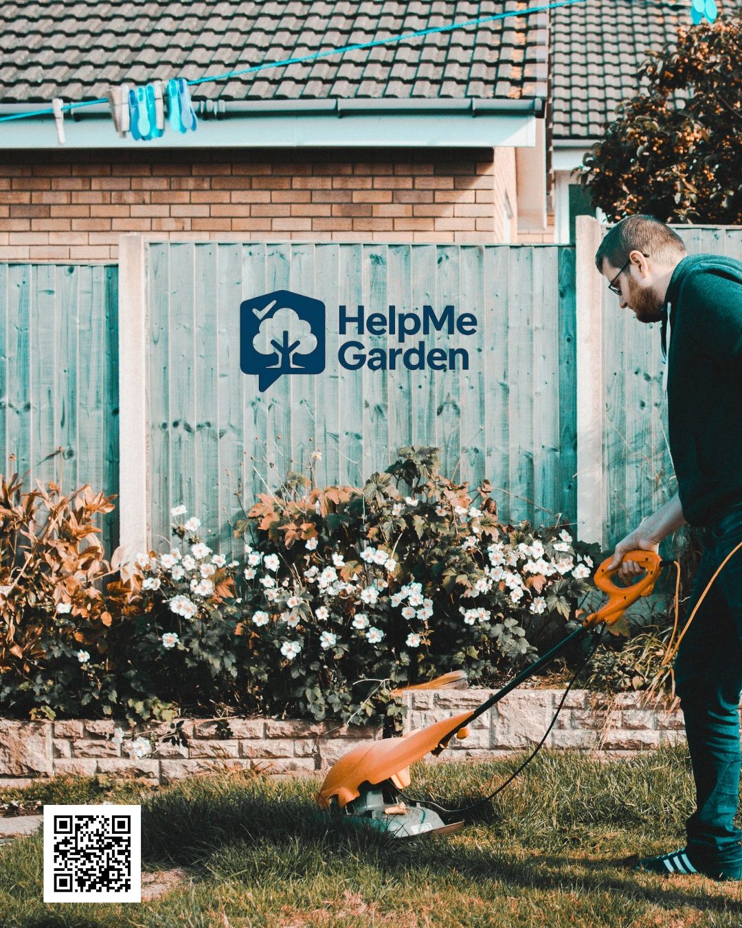 A man mowing the lawn with flowers and a wooden fence in the background.