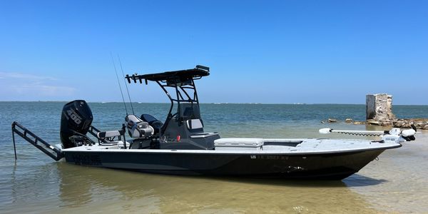 A fishing boat anchored in shallow coastal water under clear blue sky.