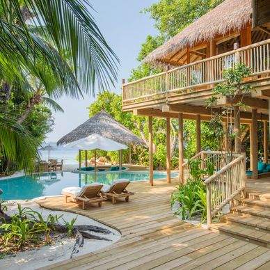 Tropical villa with pool, wooden deck, and lush greenery.