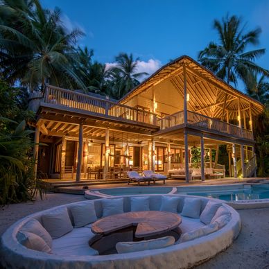 A cozy tropical villa lit warmly at dusk with a pool and sunken seating area.
