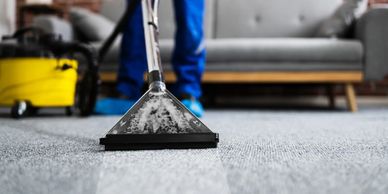 Professional carpet cleaning with steam vacuum in modern living room with grey couch and brick wall.
