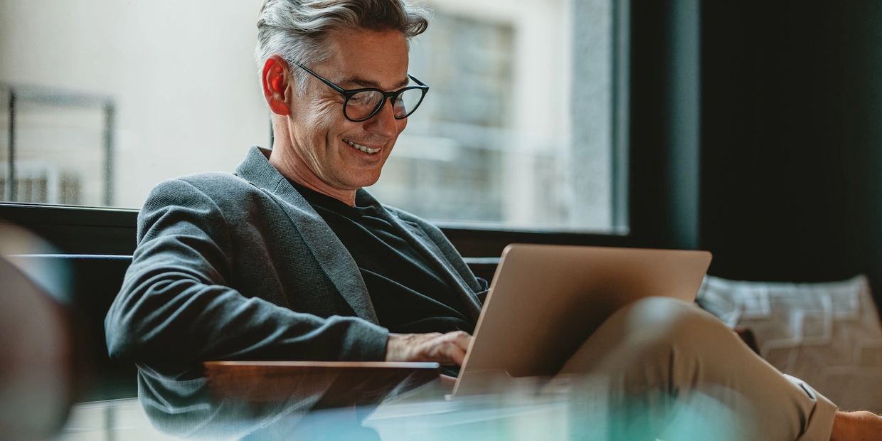 Smiling man in glasses working on a laptop in a cozy indoor setting.