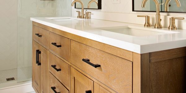 Wooden bathroom vanity with white countertop and gold faucets.