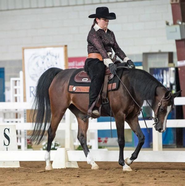 Rider in western attire guiding a horse during an indoor equestrian event.