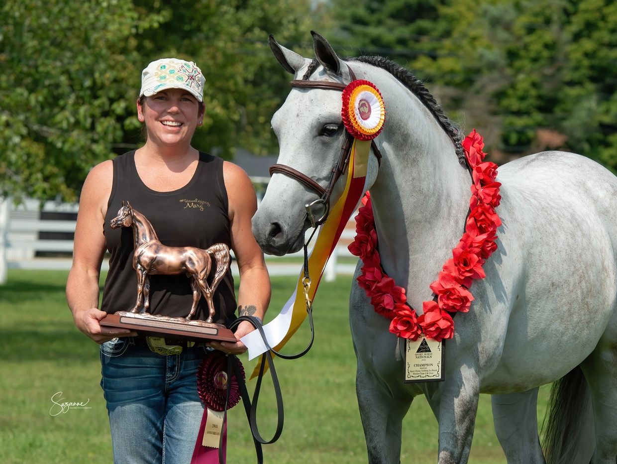 Woman holding horse trophy beside her decorated champion horse outdoors.