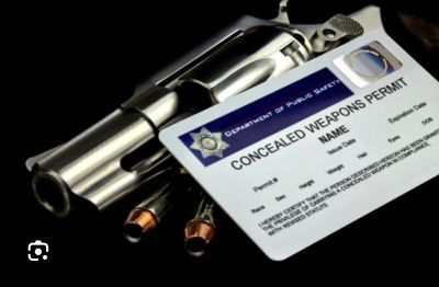A revolver partially covered by a concealed weapons permit card and bullets.