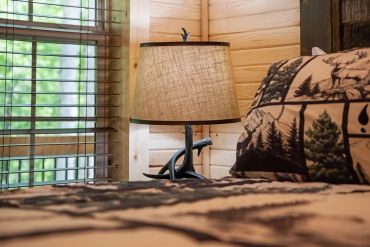 Cozy rustic bedroom corner with lamp and forest-themed bedding.