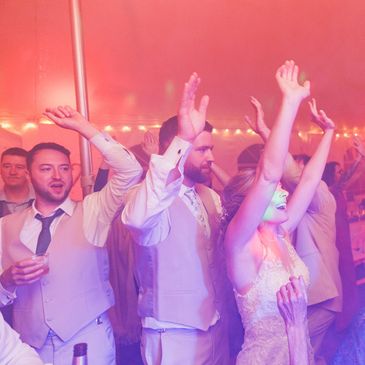 Image of bride, groom, and wedding guests dancing in haze atmospheric effects and uplighting.