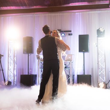 Photo of bride and groom dancing on a cloud during their wedding first dance with purple uplighting