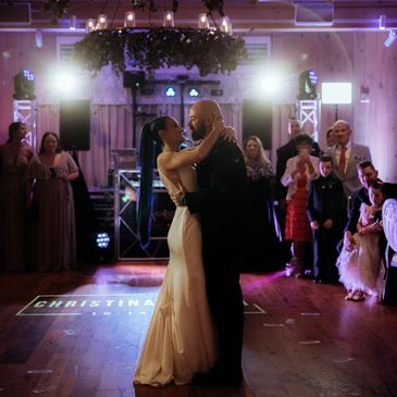 Image of bride and groom dancing during wedding first dance with custom monogram & purple uplighting.