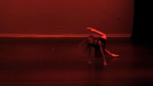 A dancer performing a move on stage under red lighting.