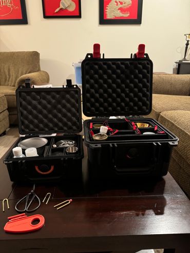 Two open black cases with various small items on a table.