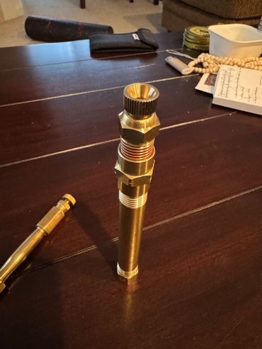 A shiny brass tool with threaded parts on a wooden table.