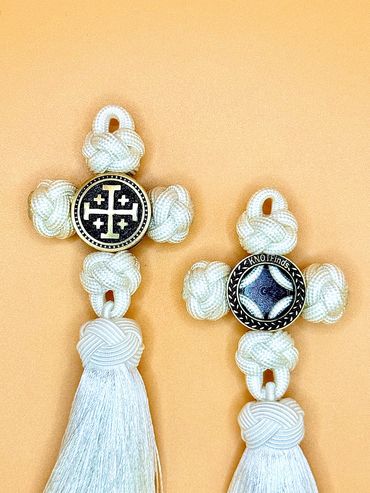 Two white knotted crosses with tassels on a peach background.
