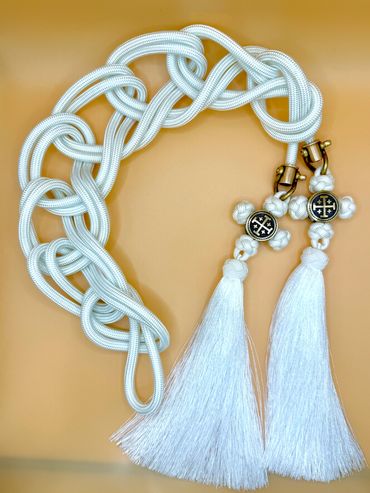 White decorative rope with tassels and cross charms on a brown surface.