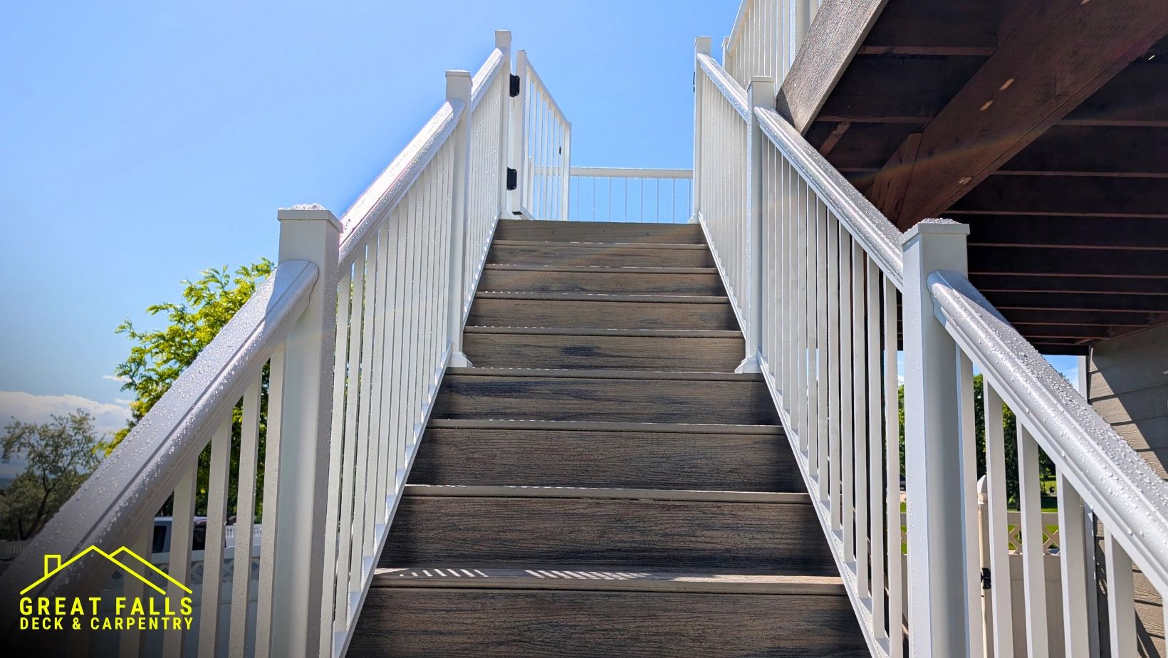 Wooden staircase with white railings under clear sky, branded with Great Falls Deck &amp; Carpentry logo.