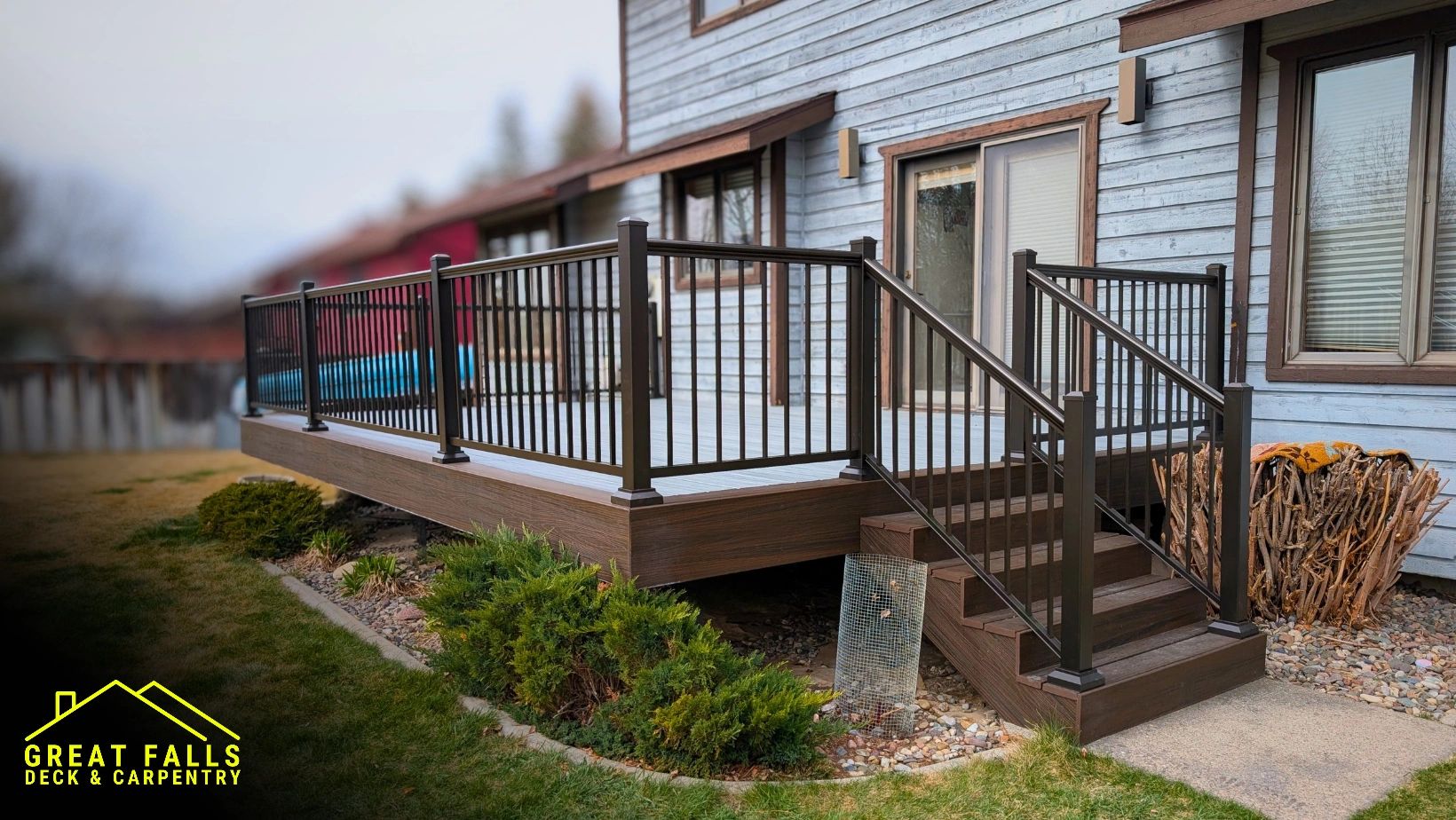 Modern wooden deck with black metal railing attached to a house.