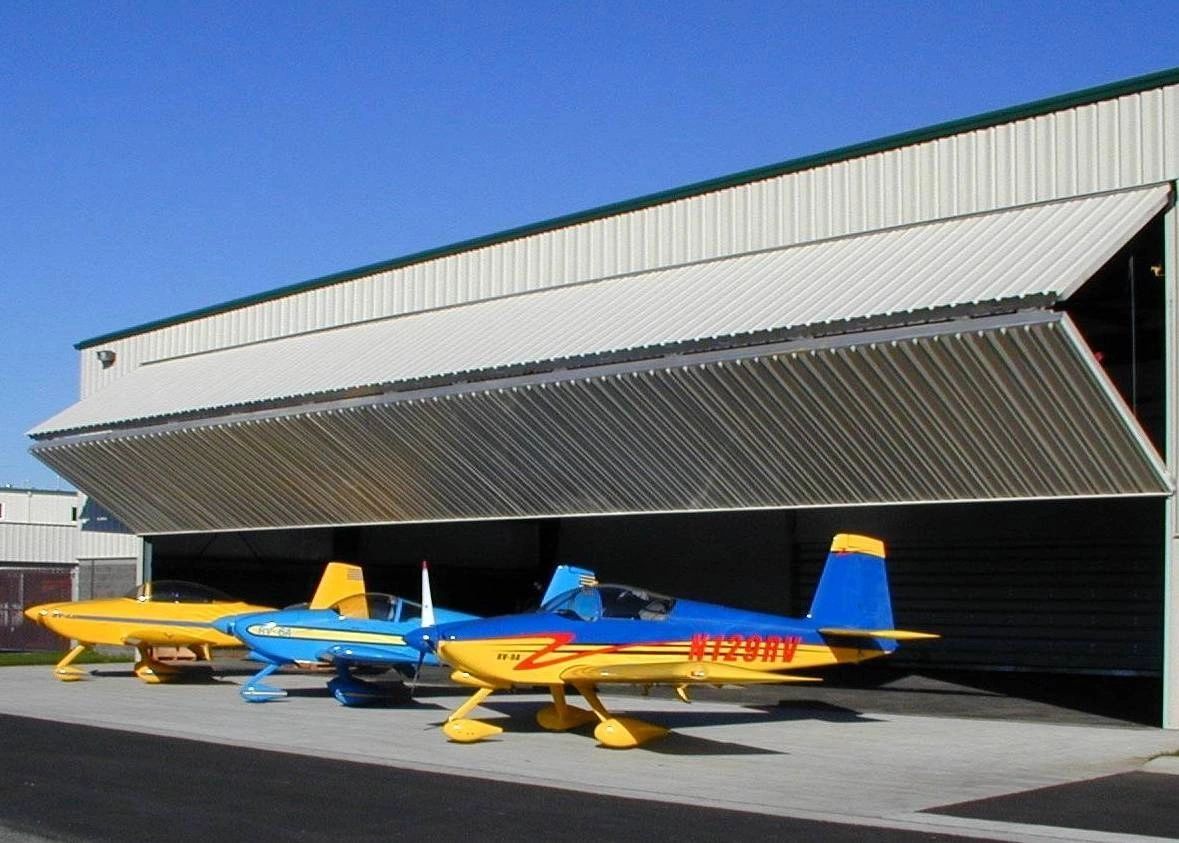 Three small colorful airplanes parked outside a hangar with an open door.