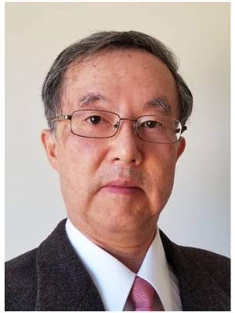 Professional portrait of an older man with glasses in a suit and pink tie.