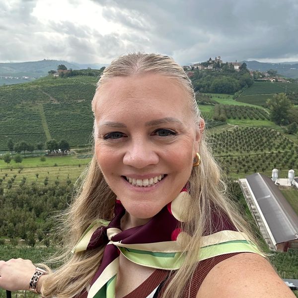 Woman smiling with scenic green hills and vineyards in the background.