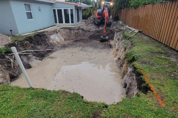 Construction site with excavator digging a large hole filled with water.