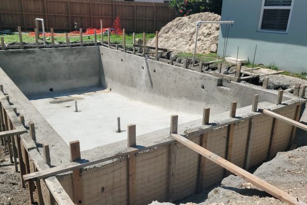 Concrete pool under construction with wooden supports and plumbing.