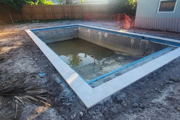 A partially constructed backyard pool with some water and surrounding dirt.