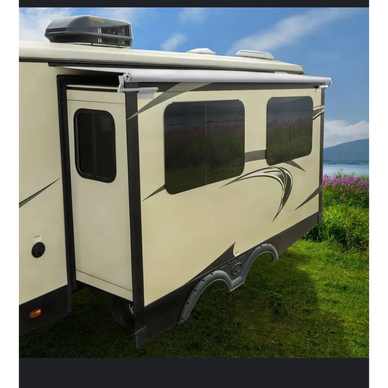 Side view of a beige RV with an extended slide-out section on green grass.