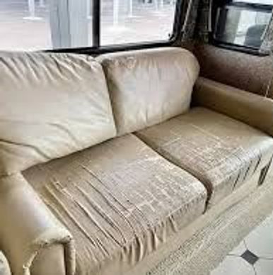 Worn-out beige sofa with cracked leather upholstery inside a room.