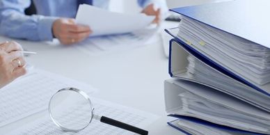Magnifying glass and binders on desk with people reviewing documents.
