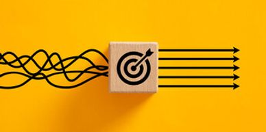 Wooden block with target symbol aligning tangled arrows into straight lines on yellow background.