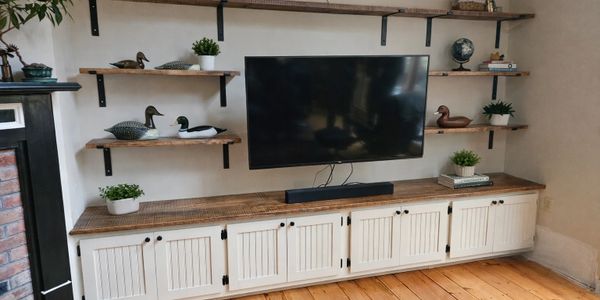 Wall-mounted TV with wooden shelves and white cabinet below, decorated with plants and duck figurines.