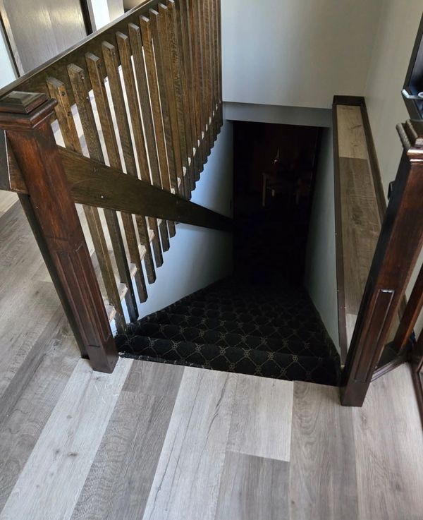 Dark staircase with wooden railing and patterned carpet.