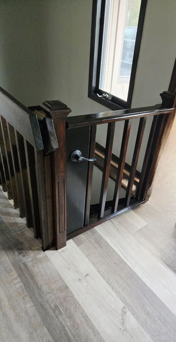 Dark wood stair railing with a gate and light-colored floor.