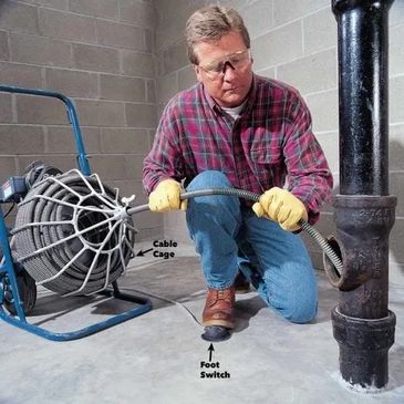 Plumber operating a sewer machine to clear a sewer stoppage