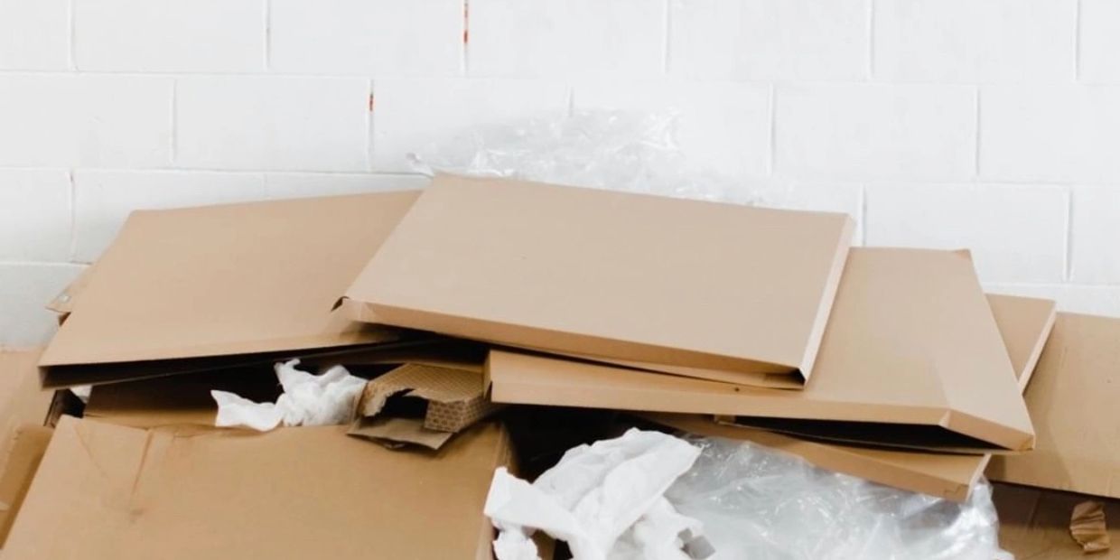 Stack of flattened cardboard boxes and packing materials against a white wall.